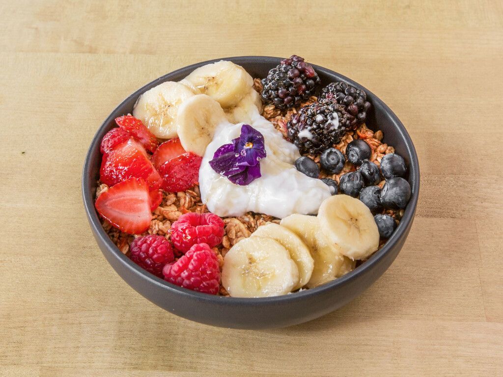 Acai bowl with granola, berries, banana slices, and a dollop of white yogurt in a black bowl.