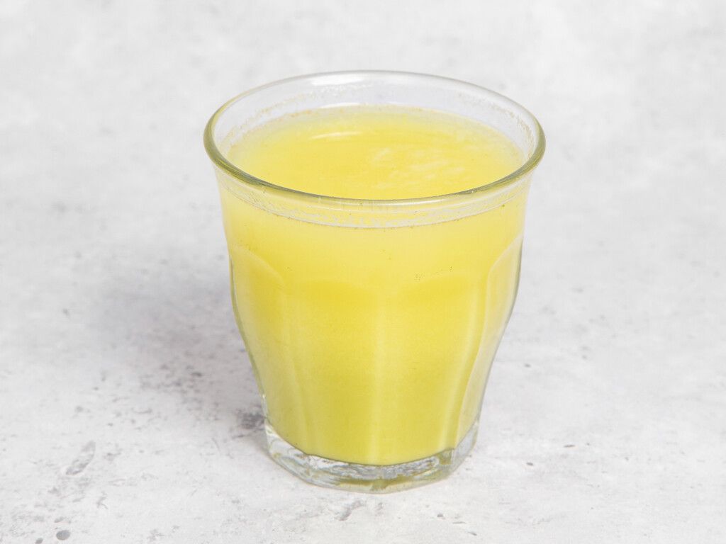 Glass of yellow liquid, likely juice, on a light gray surface.