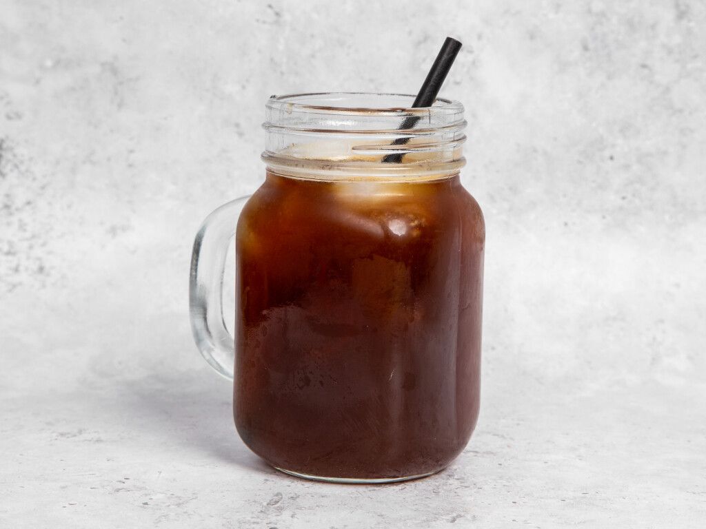 Iced coffee in a mason jar with a black straw on a light grey background.