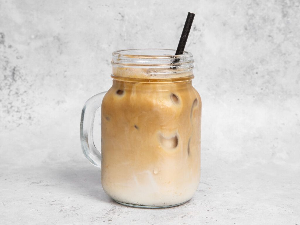 Iced coffee in a mason jar with a straw, on a light gray background.
