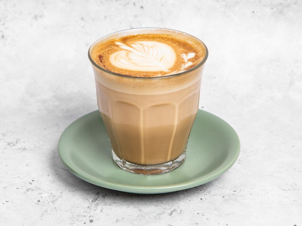 Latte in a clear glass, with latte art, on a green saucer.