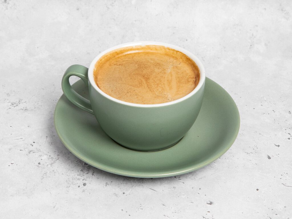 Cup of coffee in a sage green mug and saucer on a light gray background.