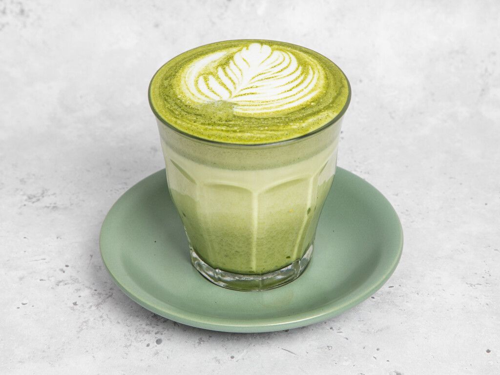 Matcha latte in glass on a green saucer, topped with leaf design.