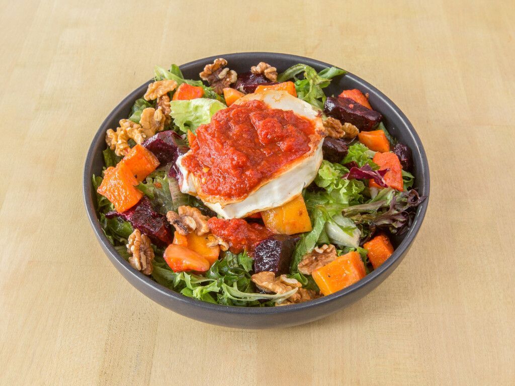 Salad with roasted vegetables, walnuts, greens, and a topping of red sauce on a white cheese block.
