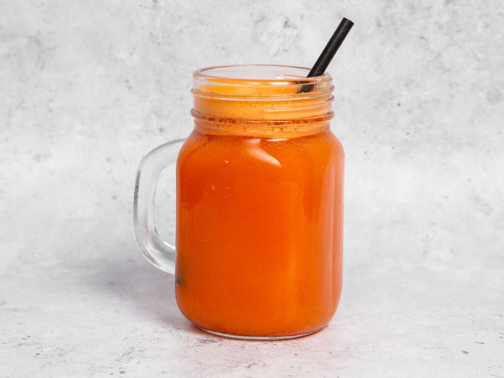 Carrot juice in a mason jar with a black straw, set against a light gray background.