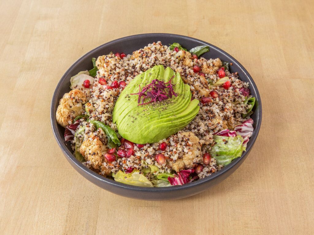 Bowl of salad with avocado, quinoa, roasted cauliflower, and pomegranate seeds.