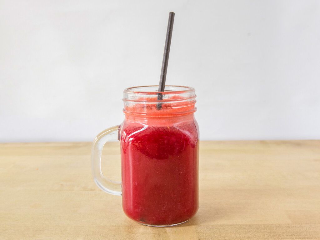 Red juice in a mason jar with a black straw, on a wooden surface.