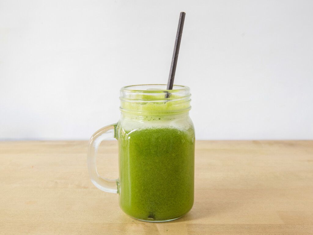 Green smoothie in a mason jar with a black straw on a wooden surface.