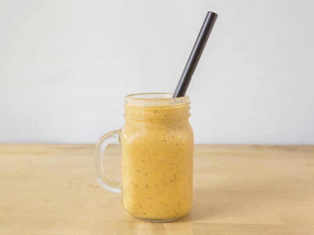 Smoothie in a mason jar with a black straw on a wooden table against a white background.
