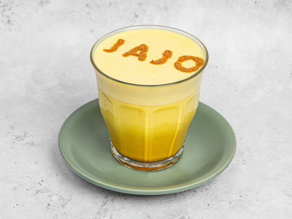 Glass of yellow beverage on a green saucer, with 
