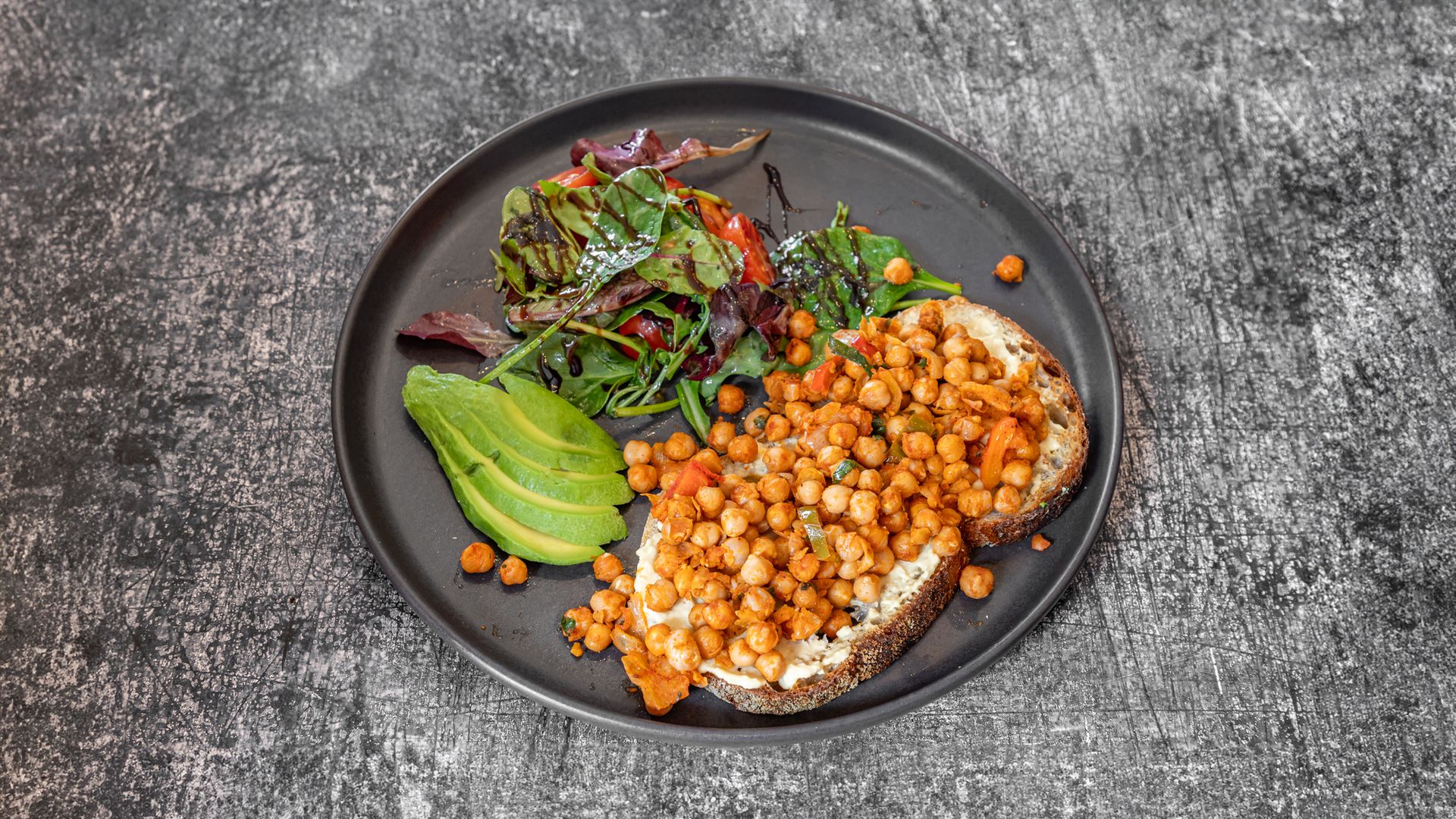 Plate with avocado, greens, and toast topped with chickpeas.
