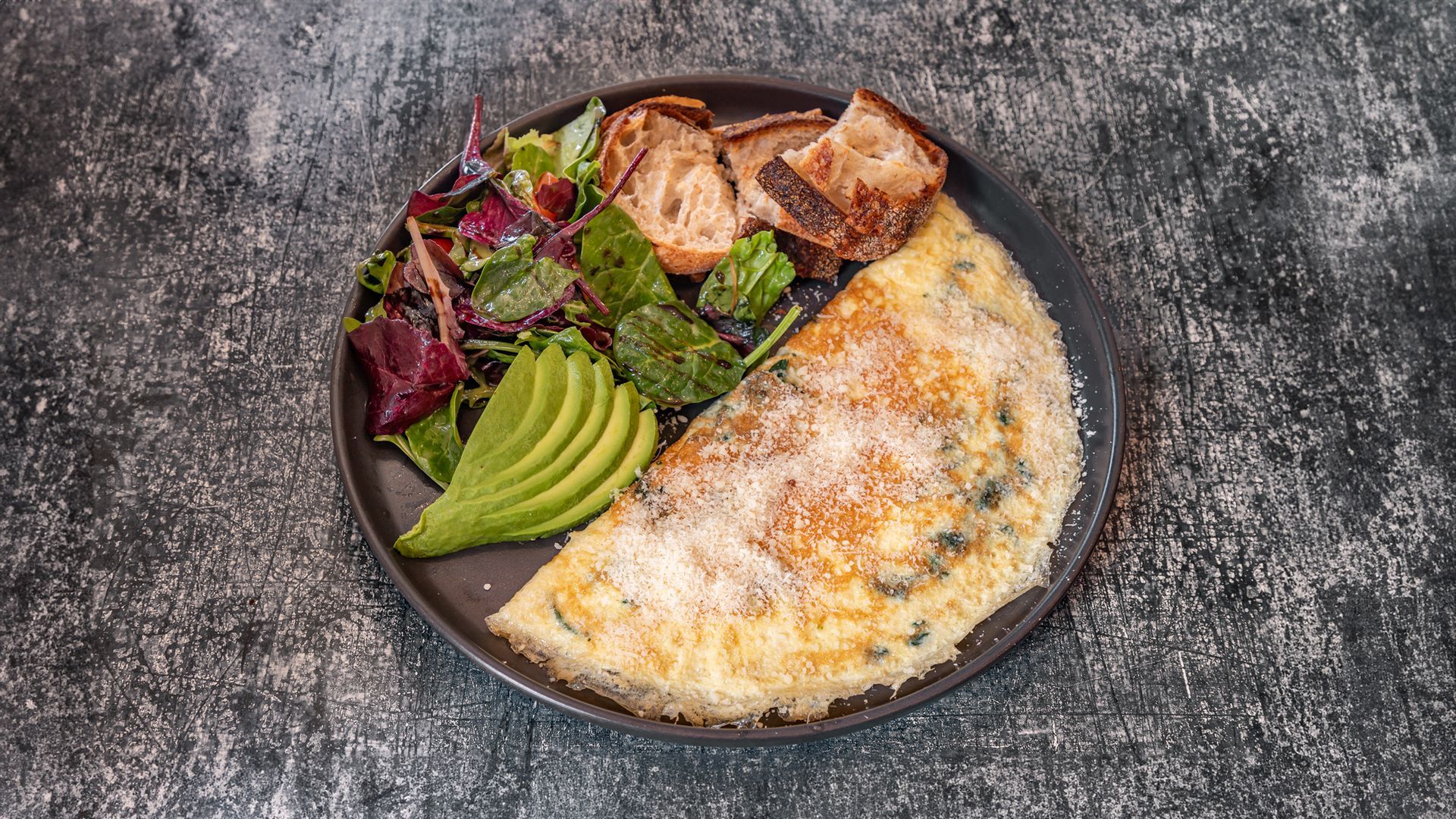 Omelet with avocado, salad, and toasted bread on a plate.