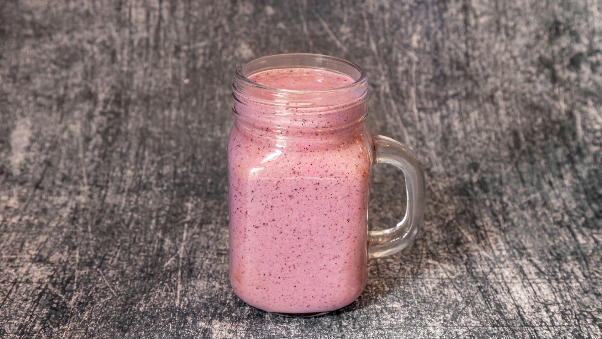 Pink smoothie in a mason jar with a handle, on a gray surface.