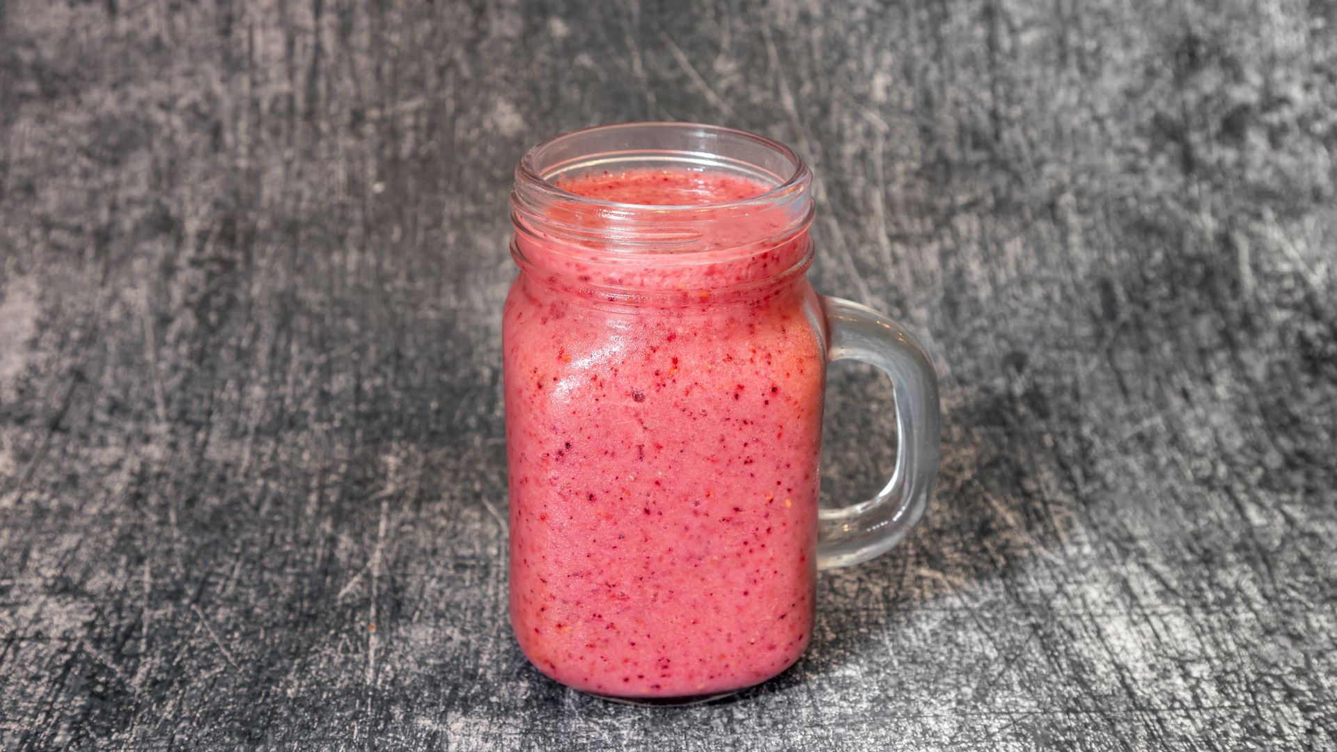 Pink smoothie in a glass jar on a gray surface.