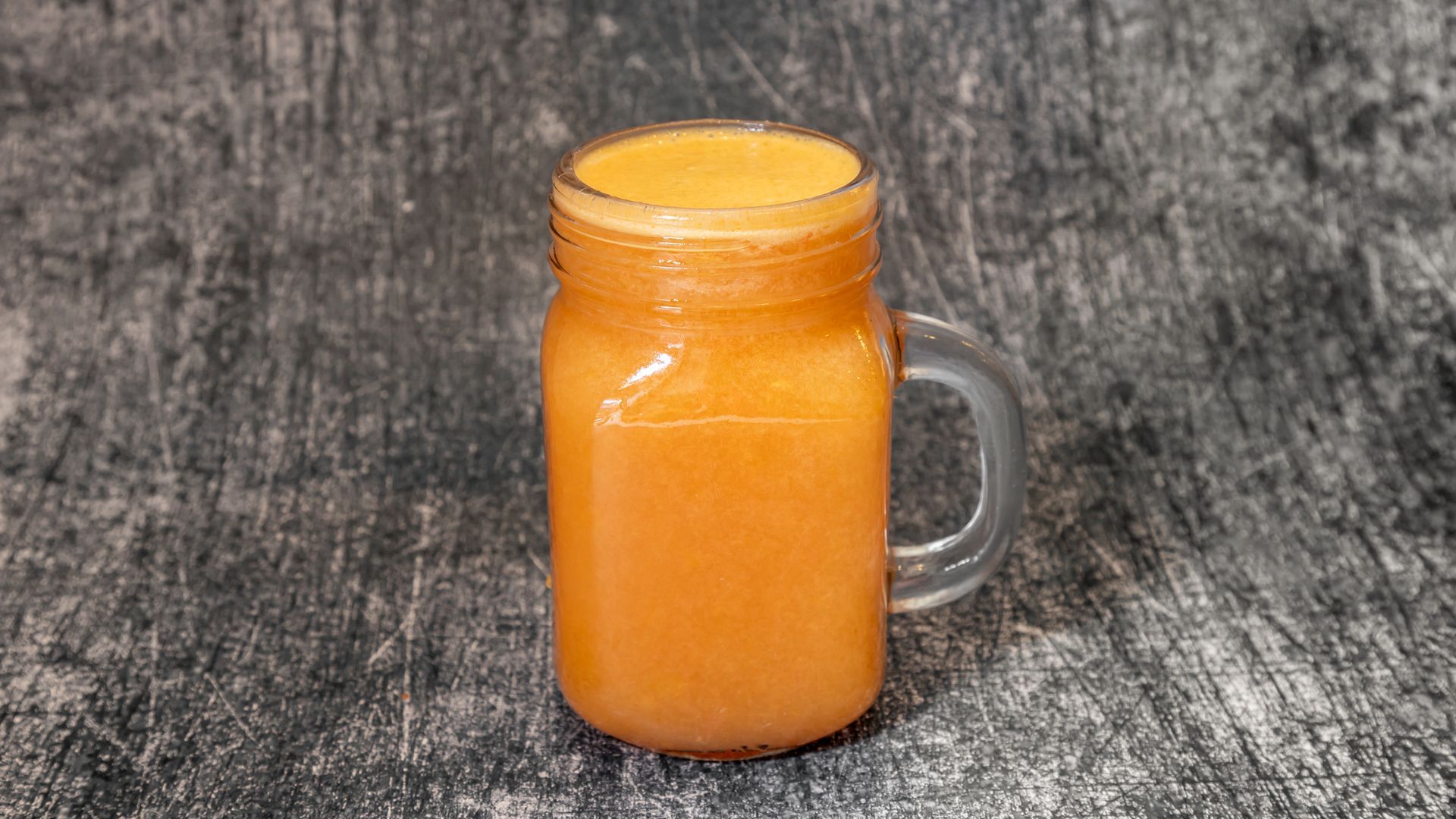 Orange juice in a mason jar with a handle, on a textured gray surface.