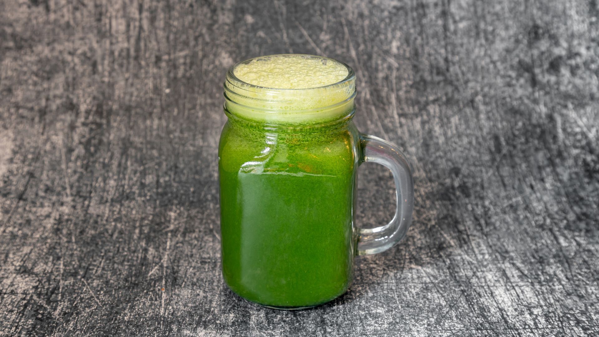 Green juice in a mason jar, sitting on a gray mottled surface.