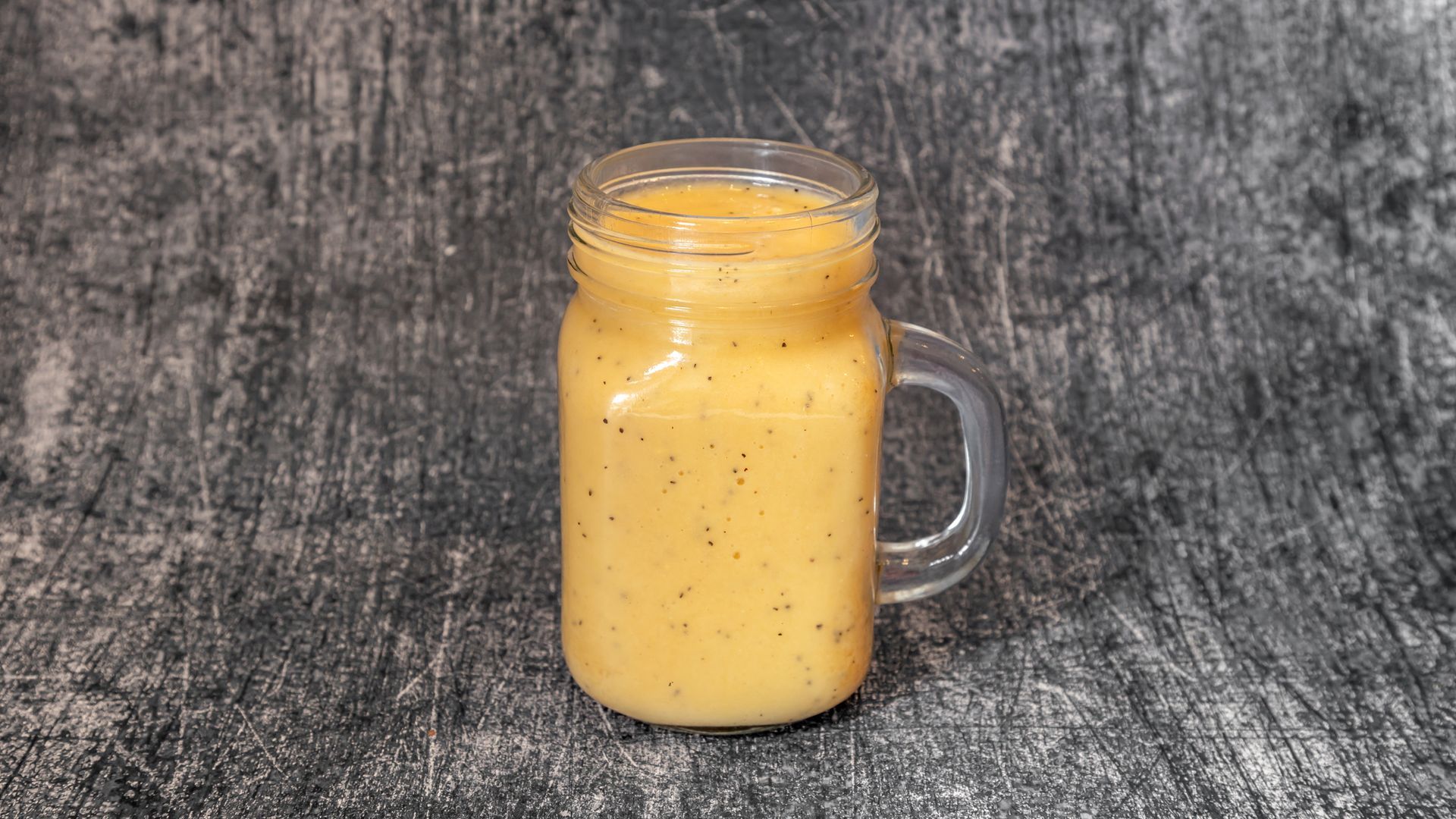 Yellow smoothie in a glass mug, placed on a gray speckled surface.