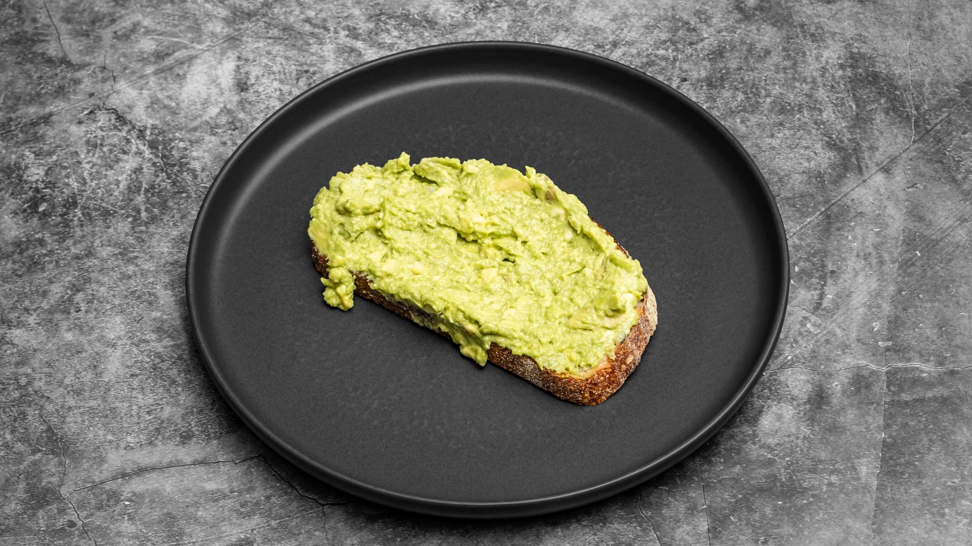 Avocado toast on a black plate, against a gray background.