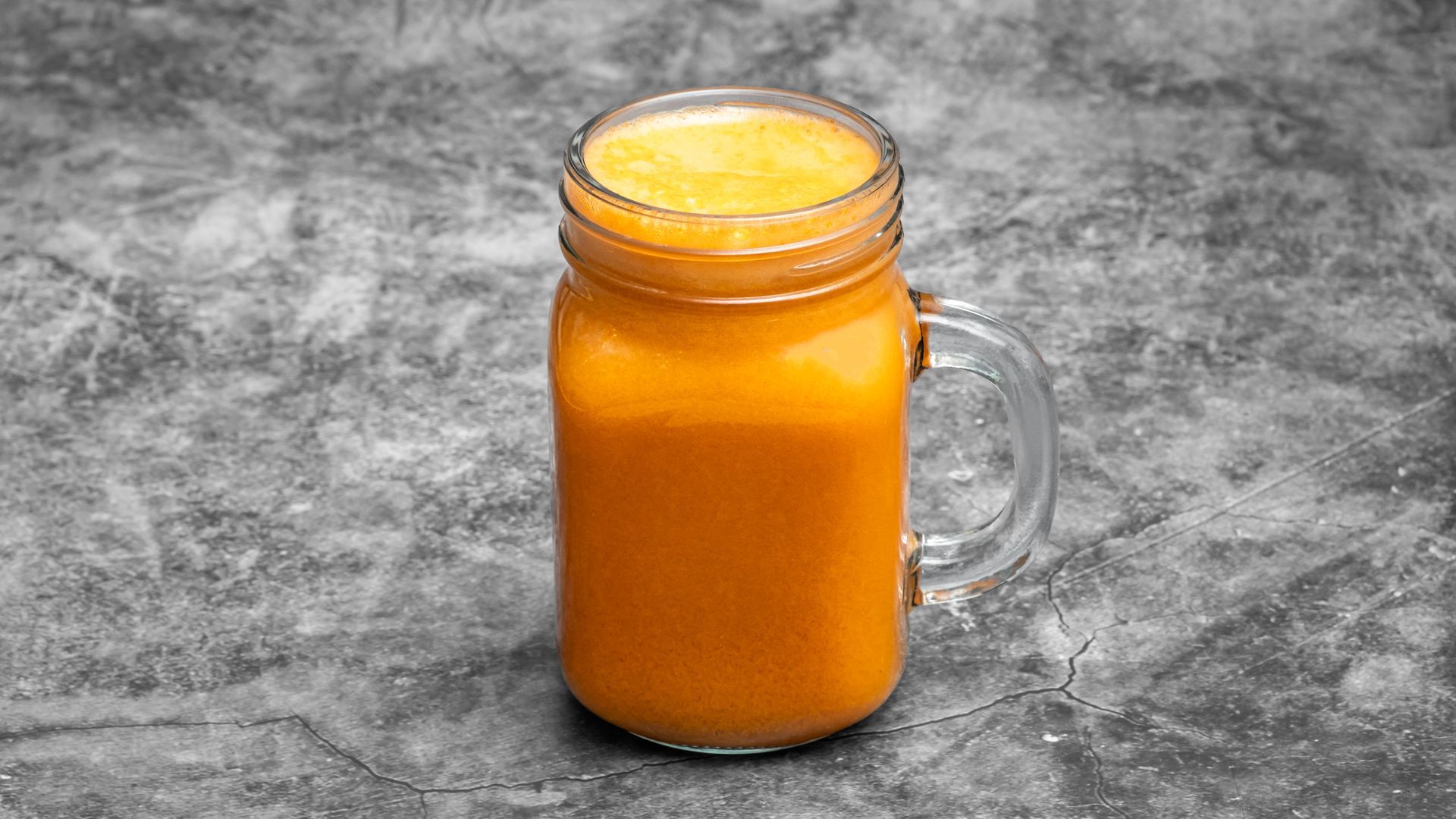 Orange juice in a mason jar, set against a gray speckled background.