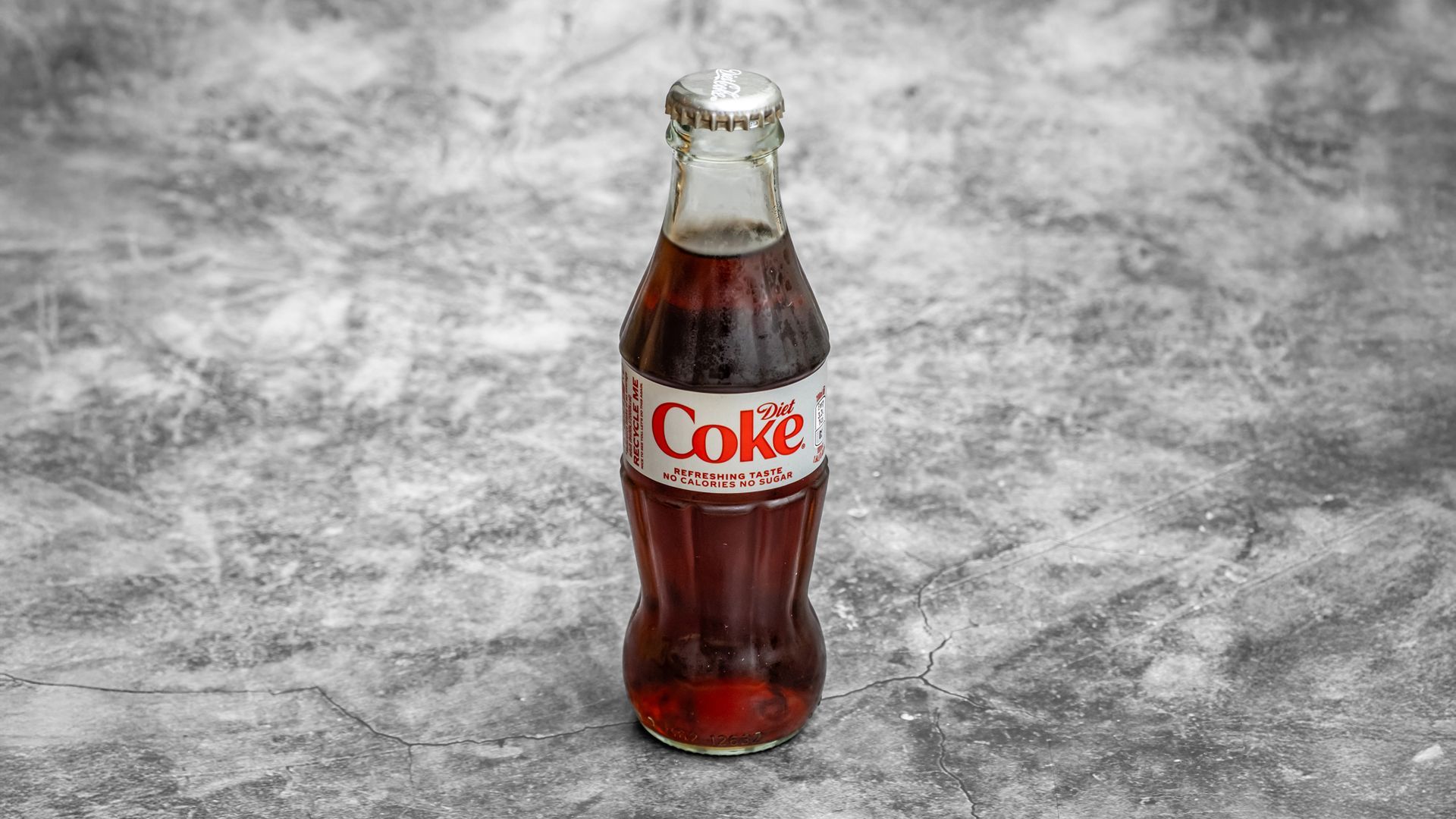 Bottle of Coca-Cola with white and red label, standing against a mottled gray background.