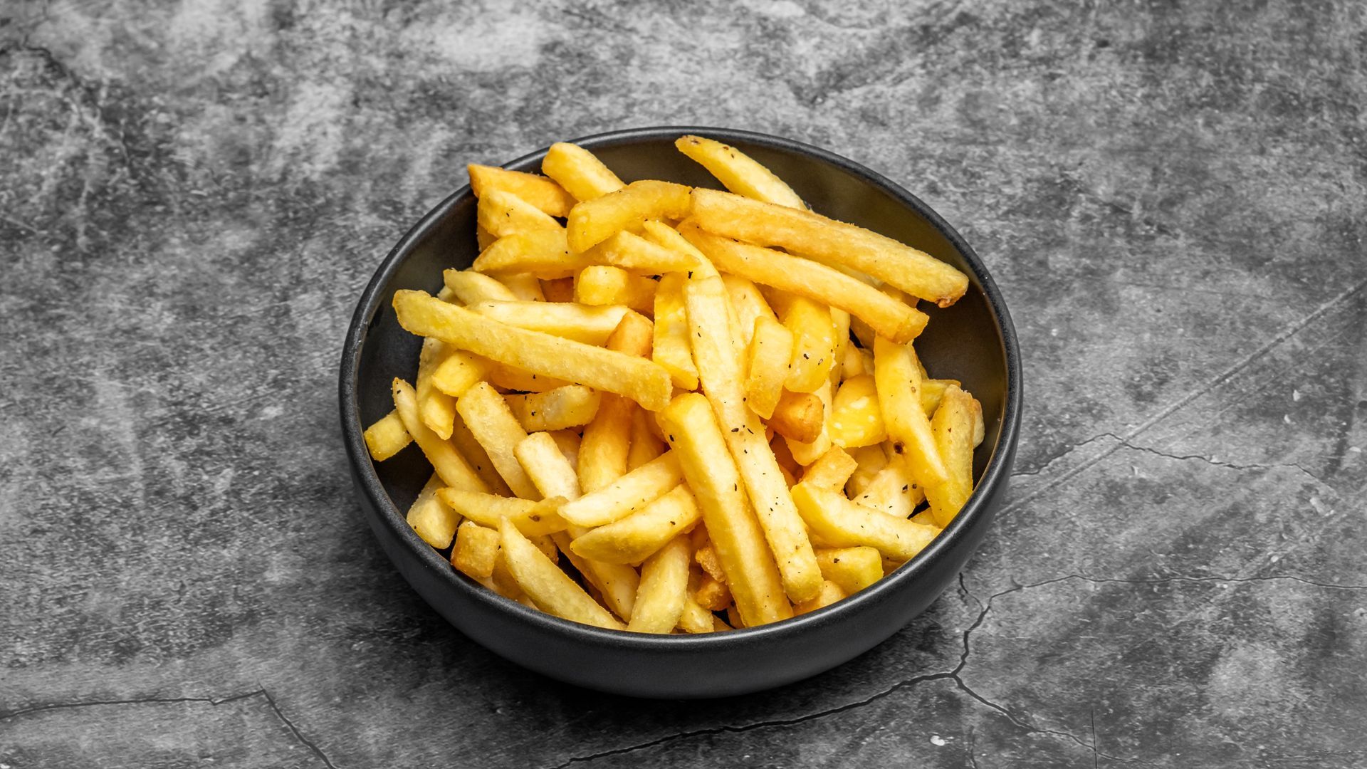 Bowl of golden french fries on a gray background.