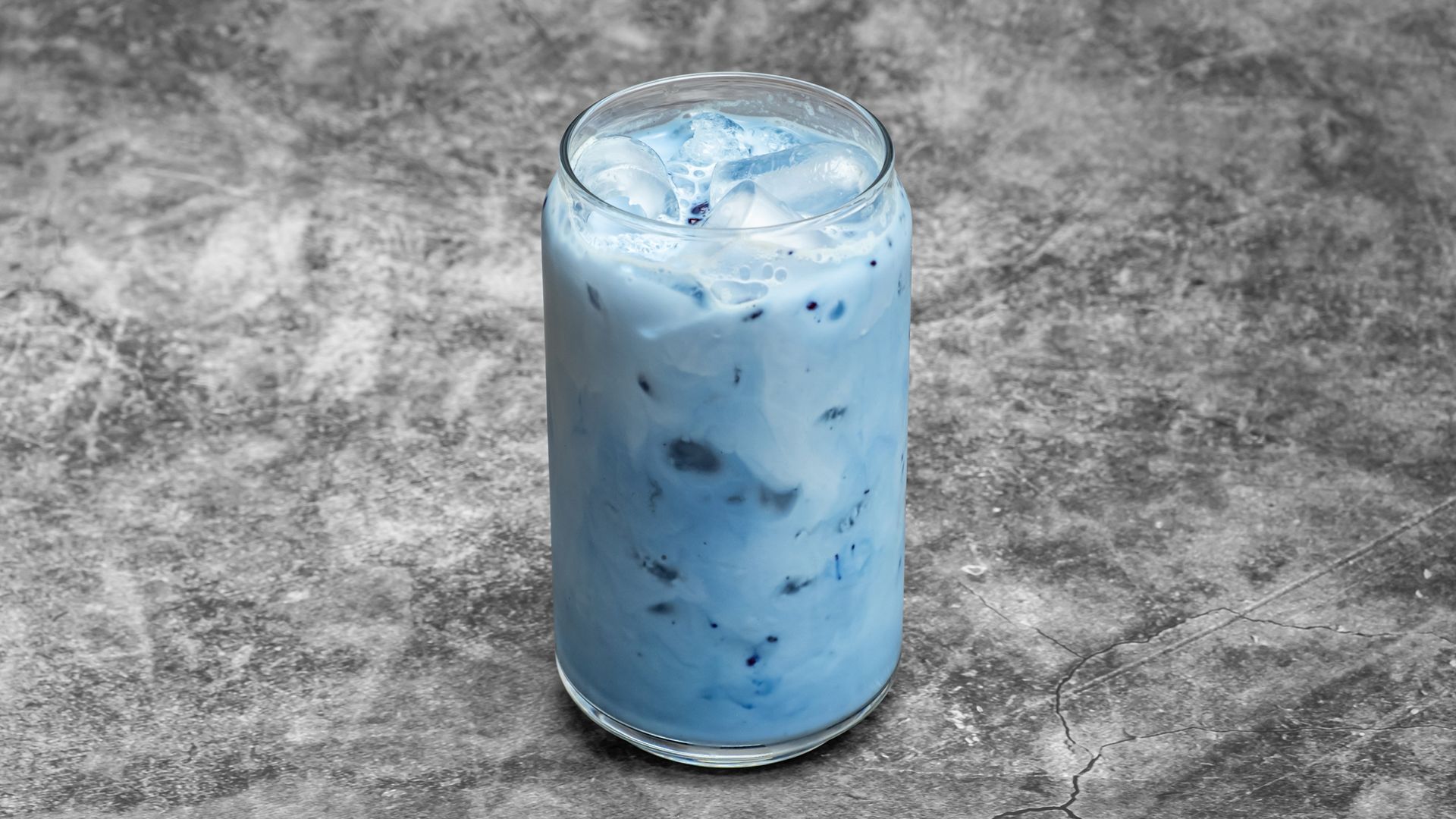 Tall glass of blue-colored iced beverage with ice cubes, set against a mottled gray background.
