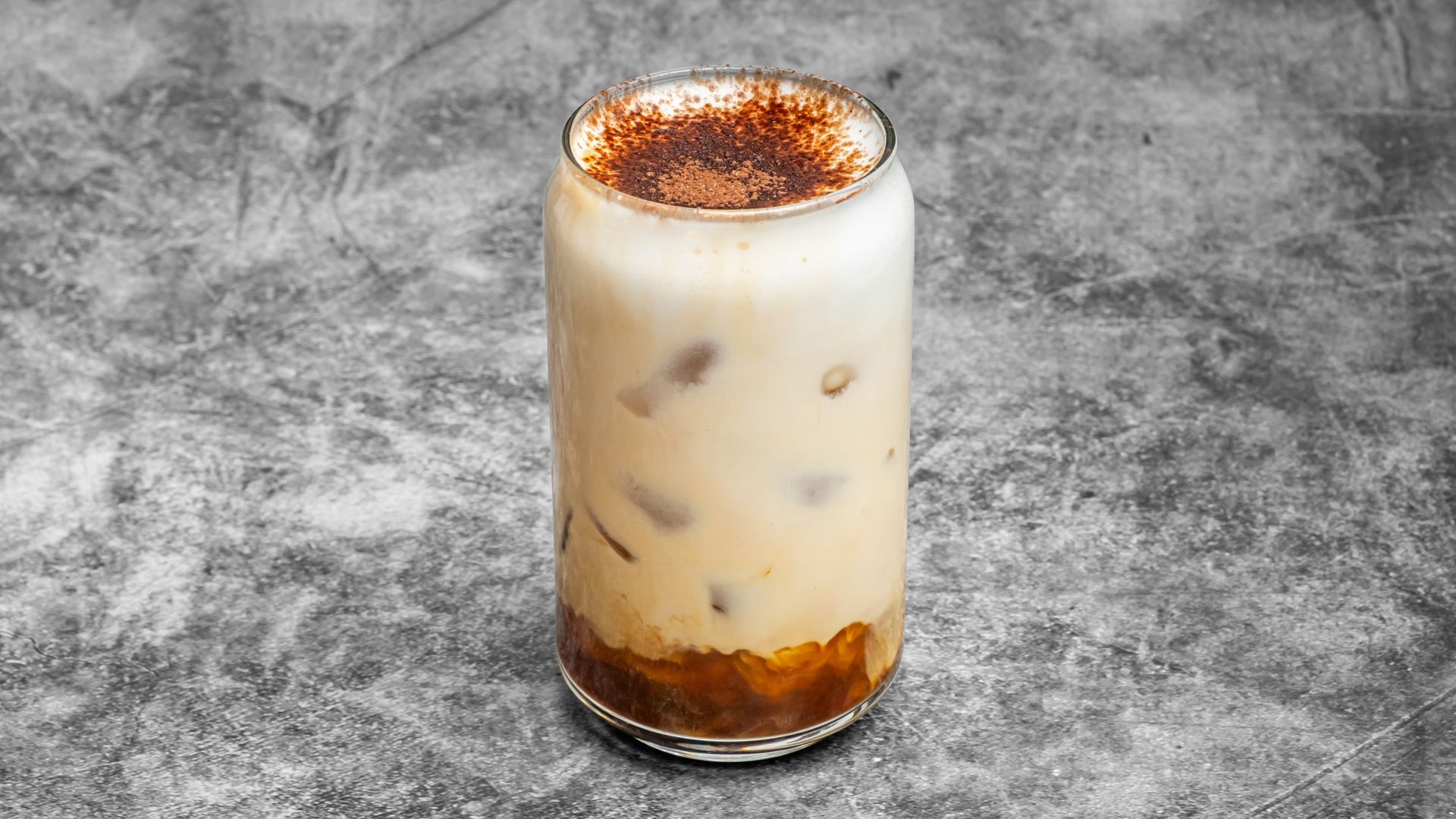 Iced coffee drink in a glass, topped with cocoa powder on a gray background.
