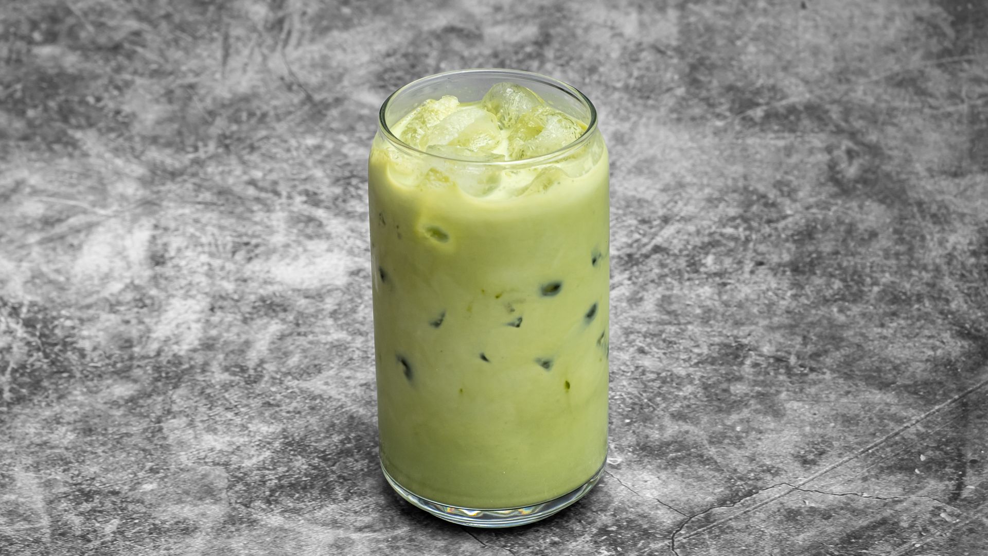 Iced matcha latte in a tall glass, on a mottled gray surface.