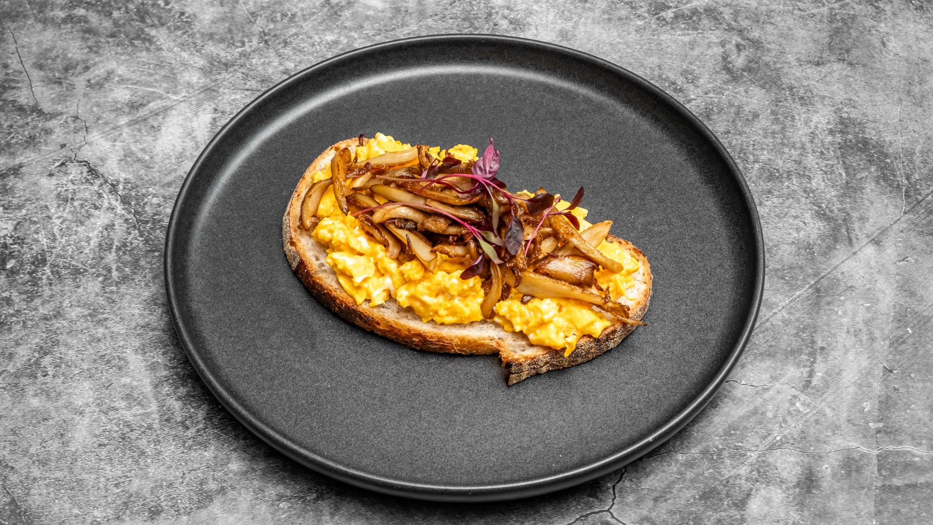 Scrambled eggs and caramelized onions on toast, served on a black plate.