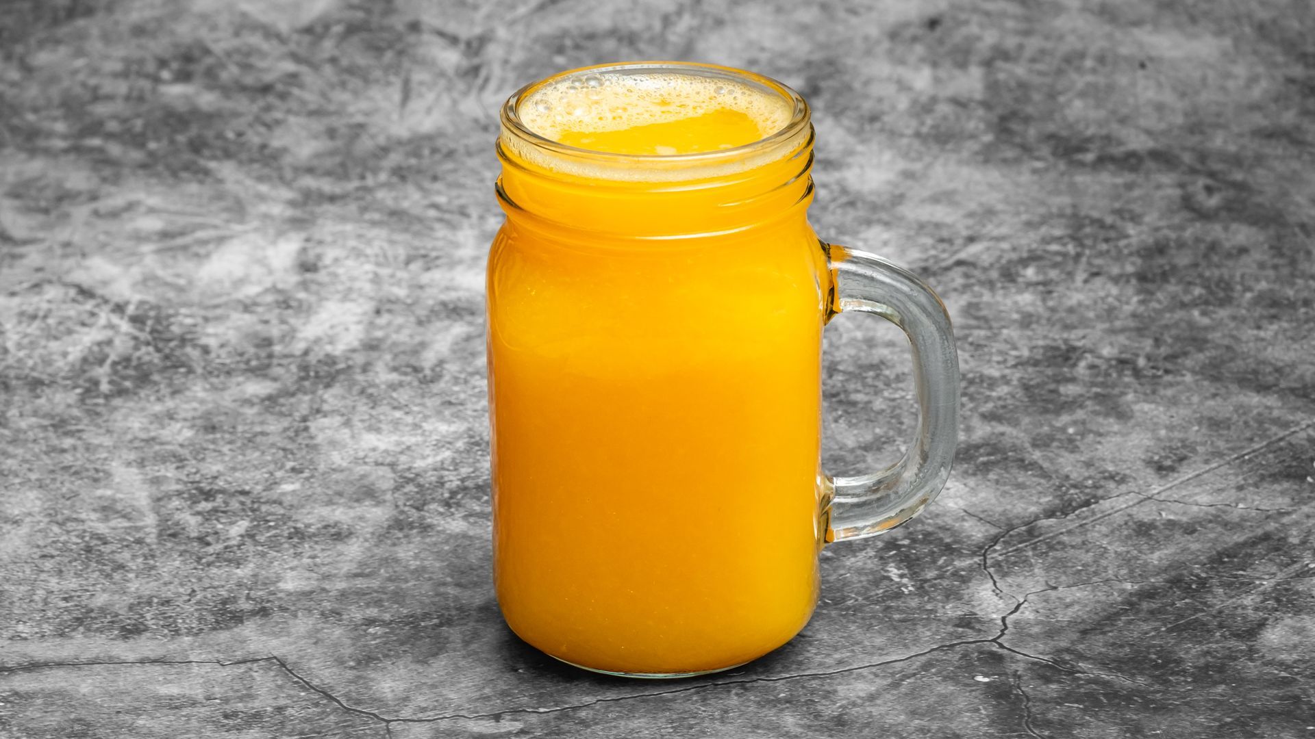 Orange juice in a mason jar against a gray mottled background.