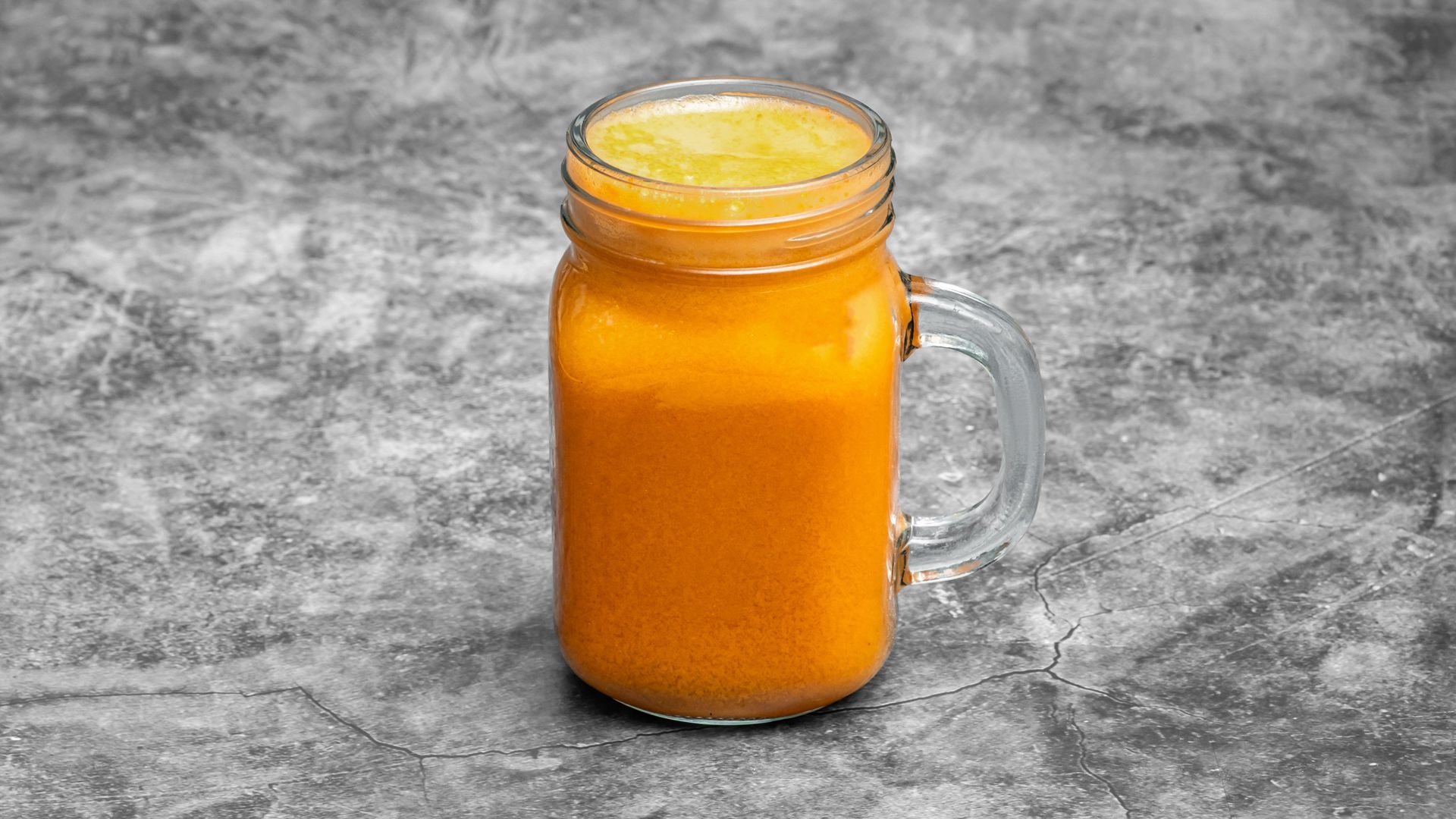 Orange juice in a mason jar with a handle; gray background.