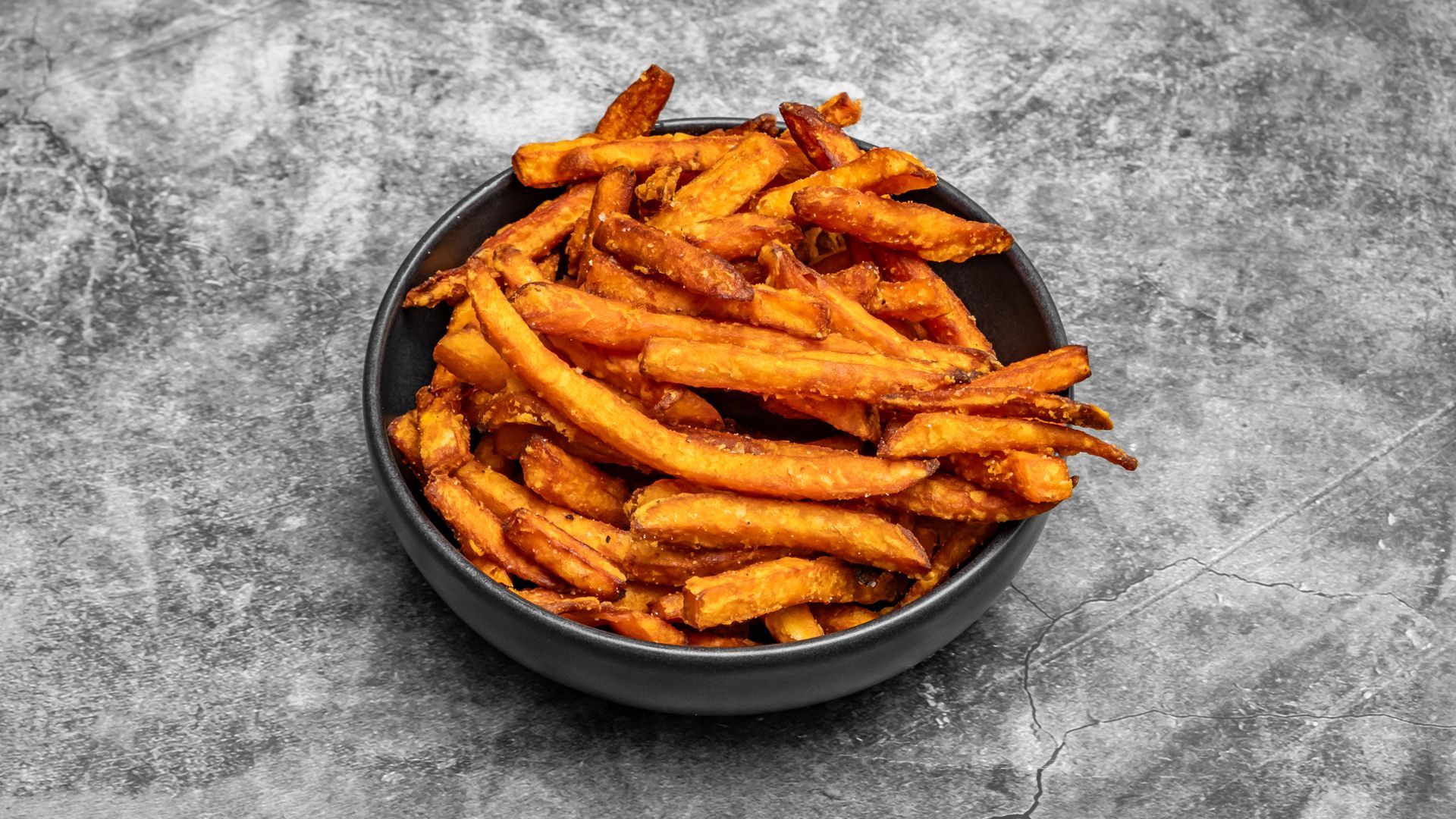 Bowl of sweet potato fries on a gray surface.