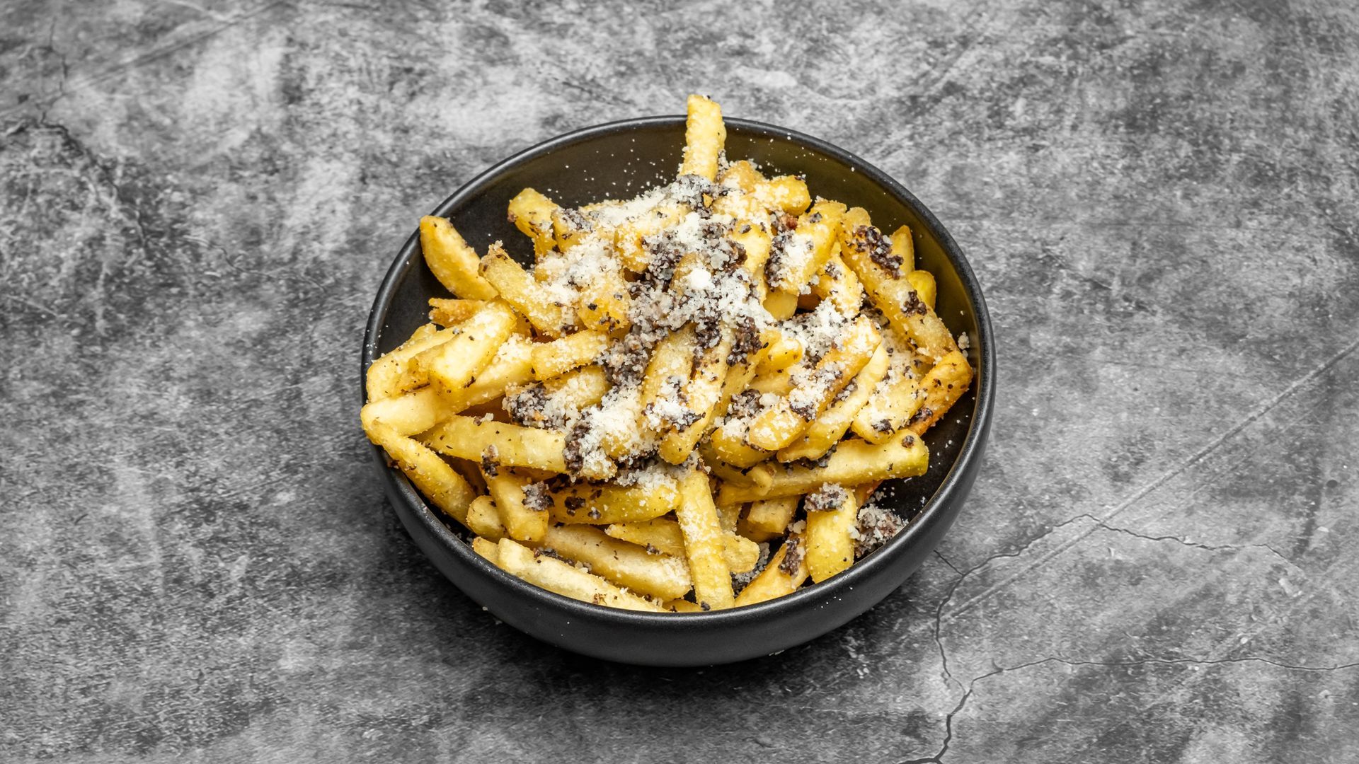 Bowl of golden french fries topped with parmesan cheese and black sesame seeds.