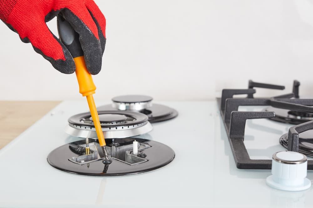 A Person Is Fixing a Gas Stove with A Screwdriver — Origin Plumbing & Gas in Tuckurimba, NSW