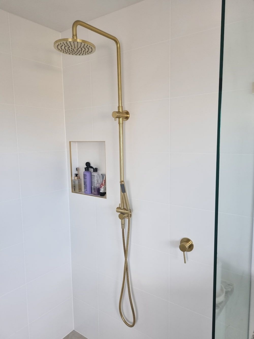 A Shower with A Gold Shower Head and A Glass Door — Origin Plumbing & Gas in Tuckurimba, NSW