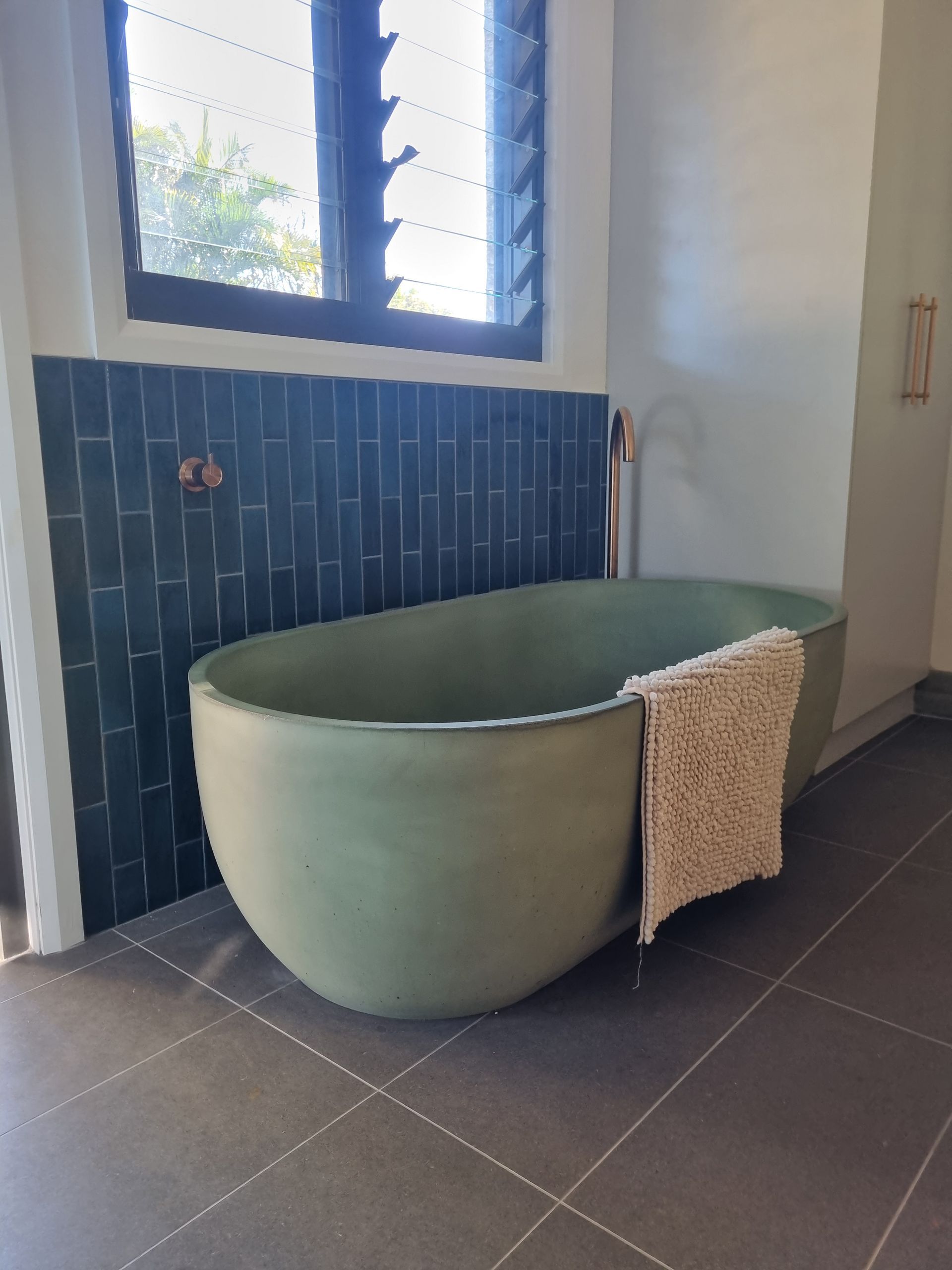 A Green stone bathtub is against a blue tiled wall — Origin Plumbing & Gas in Tuckurimba, NSW