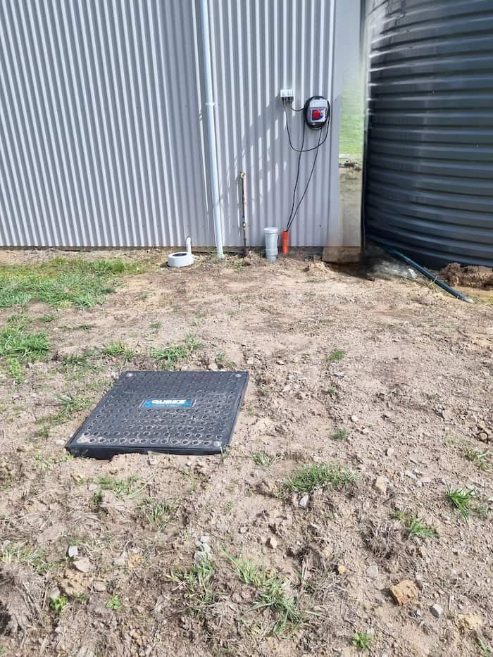 A Black Box Is Sitting in The Dirt in Front of A Building — Origin Plumbing & Gas in Tuckurimba, NSW