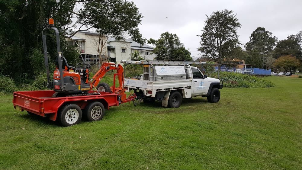 A Truck Is Towing a Trailer with A Small Excavator on It — Origin Plumbing & Gas in Tuckurimba, NSW