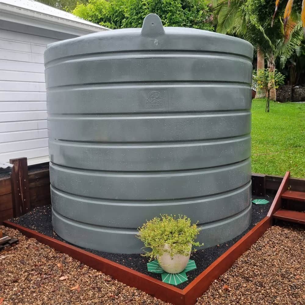 A Large Grey Water Tank Is Sitting on A Gravel — Origin Plumbing & Gas in Tuckurimba, NSW