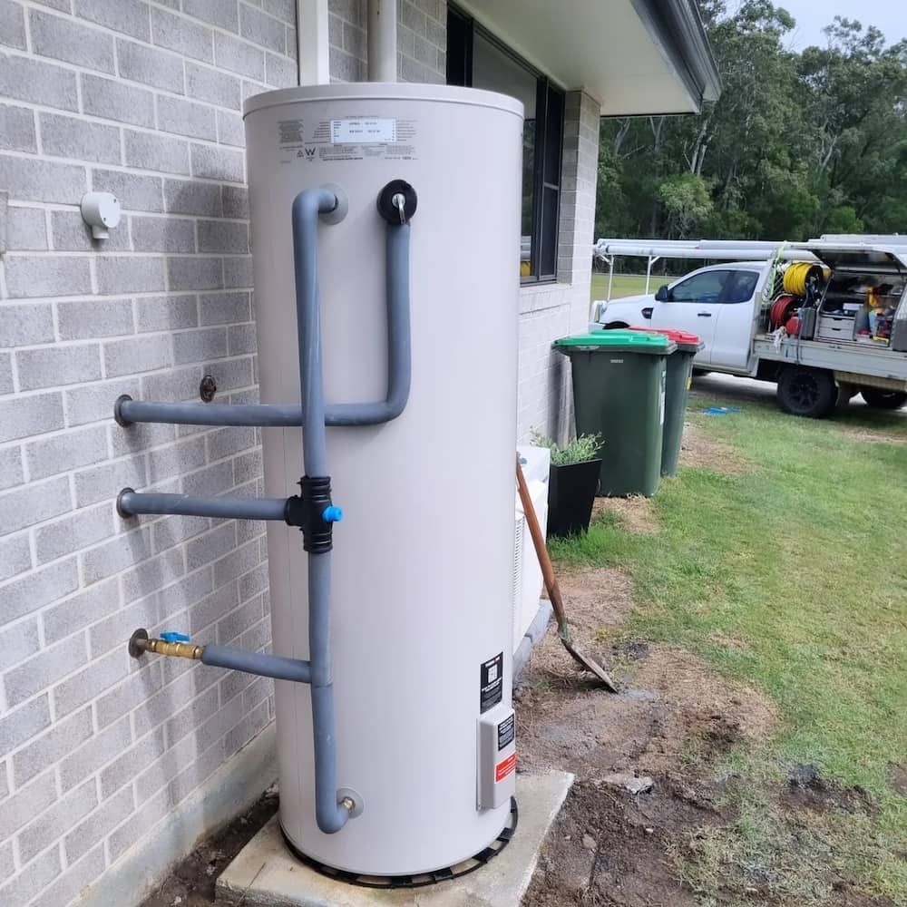 A White Water Heater Is Sitting on The Side of A Brick Building — Origin Plumbing & Gas in Alstonville, NSW