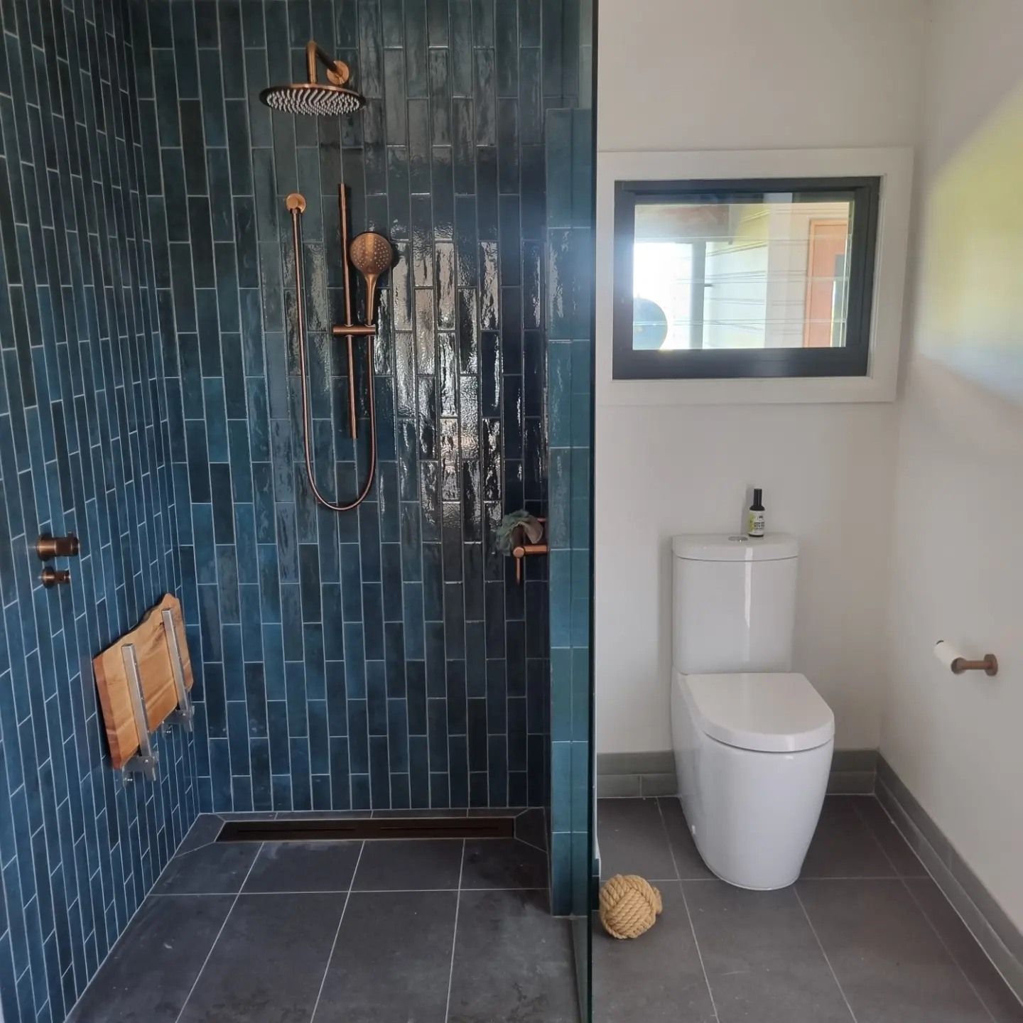 A Bathroom with a toilet and a blue tiled shower with gold tapware — Origin Plumbing & Gas in Tuckurimba, NSW
