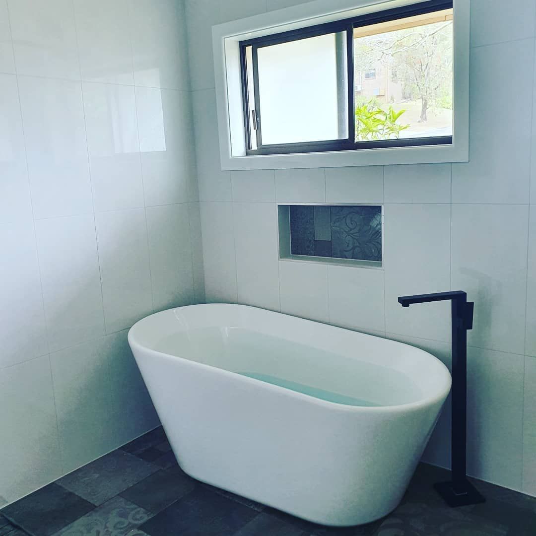 A White Bathtub Is Sitting in A Bathroom Next to A Window — Origin Plumbing & Gas in Tuckurimba, NSW