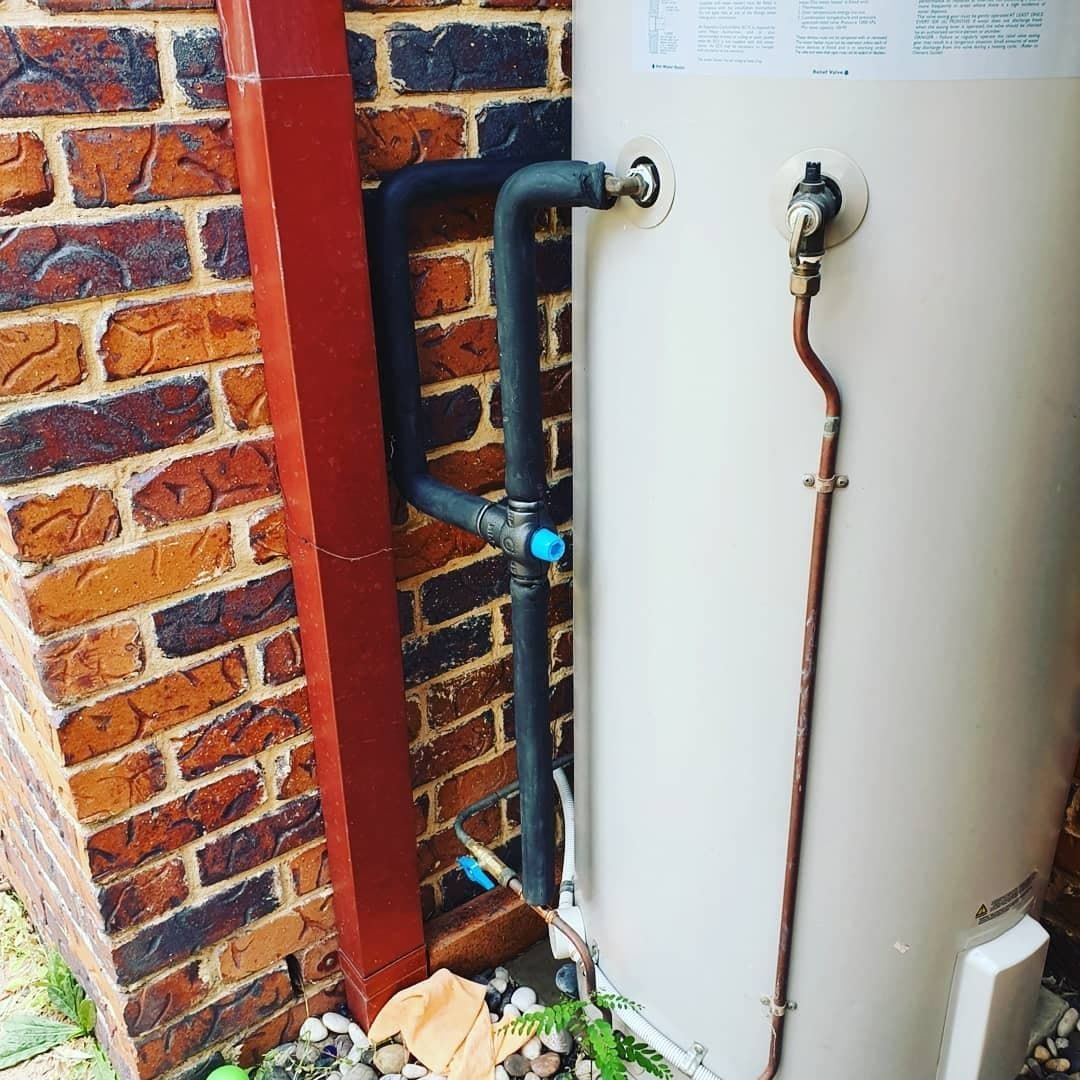 A White Water Heater Is Attached to A Brick Wall — Origin Plumbing & Gas in Tuckurimba, NSW