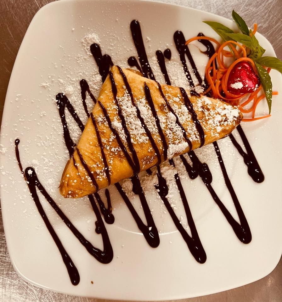 A White Plate Topped With a Piece of Food With Chocolate Sauce and Powdered Sugar — Thai Taste Restaurant In Gracemere, QLD