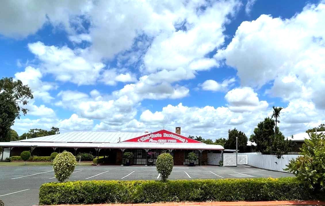 A Large White Building With a Red Roof is Surrounded by Trees and Bushes — Thai Taste Restaurant In Norman Gardens, QLD