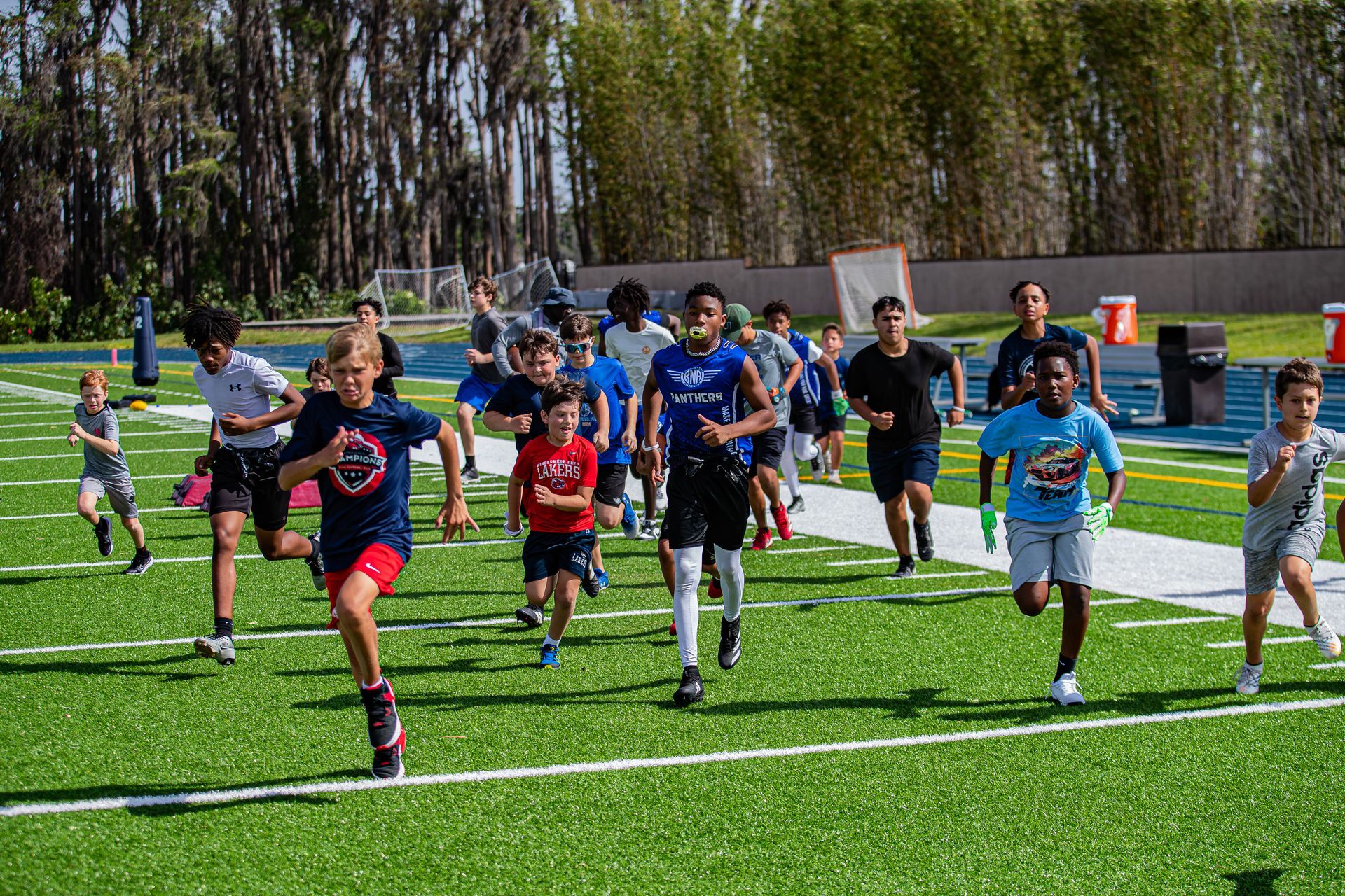 A group of people wearing athletic clothing run together across a green sports field on a sunny day.
