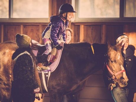 A woman is standing next to a child riding a horse