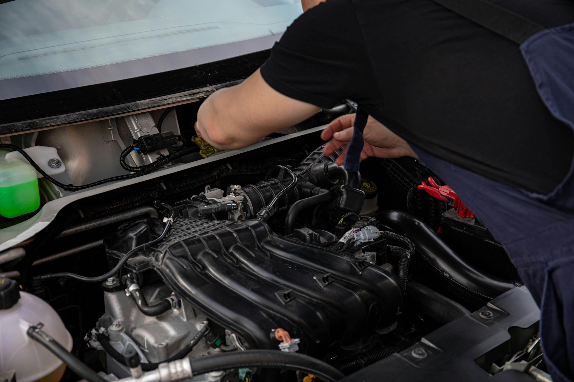 Mechanic working in a car engine bay with a red tool under the hood