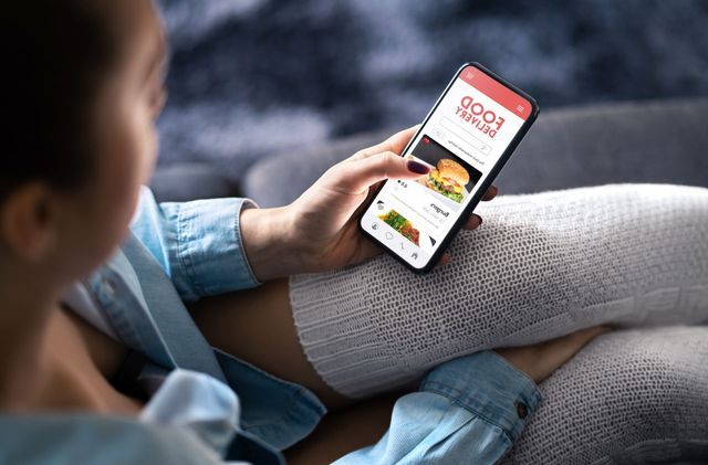 Woman holding a phone, browsing a food delivery app while sitting on a couch.