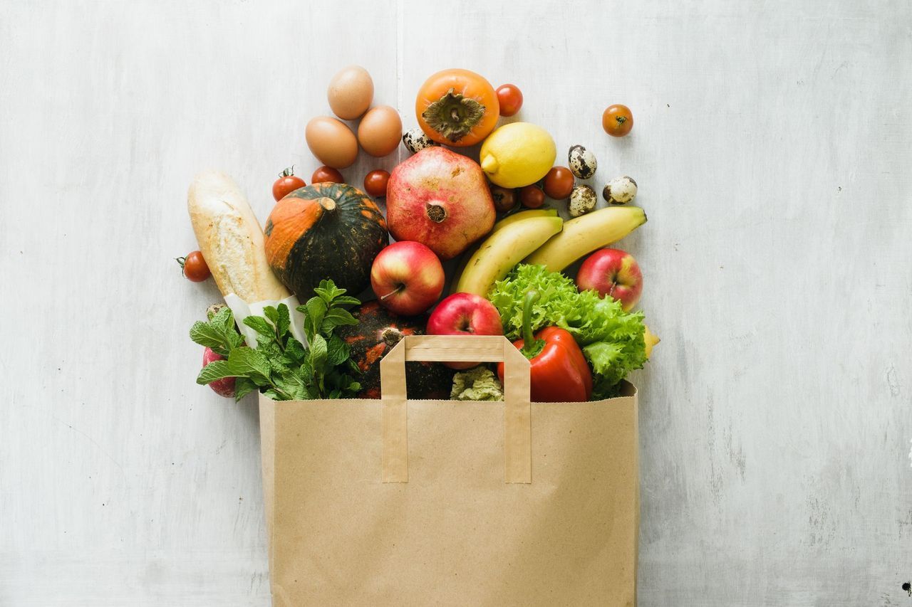 Paper grocery bag overflowing with colorful fruits and vegetables.
